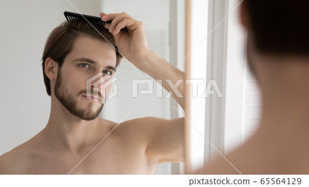 Young Caucasian man brush style hair in bathroom 65564129