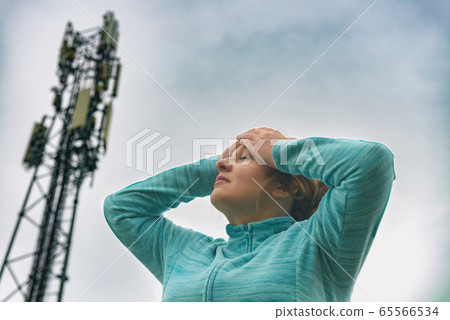 Woman is holding her head near the 5G BTS 65566534