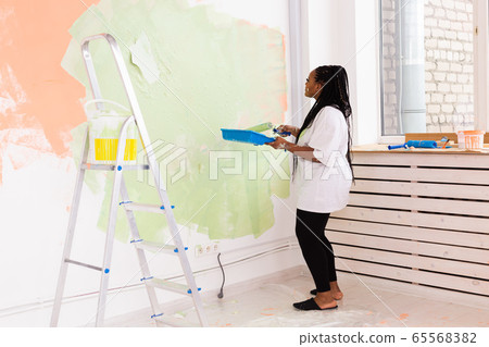 Lovely african american housewife painting wall. Renovation, redecoration and repair concept. Lovely african american housewife painting wall. Renovation, redecoration and repair concept. 65568382