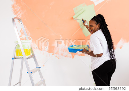 Smiling african american woman painting interior wall of home. Renovation, repair and redecoration concept. 65568392