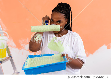 Angry african american woman painting interior wall of new house. Redecoration, renovation, apartment repair and refreshment concept. Angry african american woman painting interior wall of new house. Redecoration, renovation, apartment repair and refreshment concept. 65568397