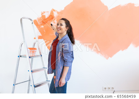 Happy smiling woman painting interior wall of new house. Redecoration, renovation, apartment repair and refreshment concept. Copy space. Happy smiling woman painting interior wall of new house. Redecoration, renovation, apartment repair and refreshment concept. Copy space. 65568459