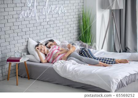 Dark-haired bearded man hugging his pregnant wife while sleeping 65569252