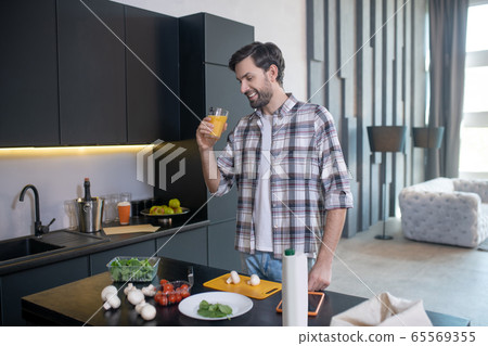 Smiling man with glass of juice standing near the table. Smiling man with glass of juice standing near the table. 65569355