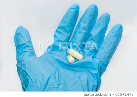 White long capsules pills on hand in blue glove 65571475