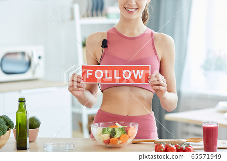 Fit Young Woman Holding Follow Sign in Kitchen 65571949