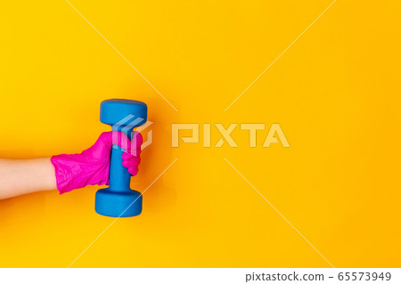 Hand in pink rubber glove holding dumbbell, gym weight isolated on yellow studio background with copyspace. Hand in pink rubber glove holding dumbbell, gym weight isolated on yellow studio background with copyspace. 65573949
