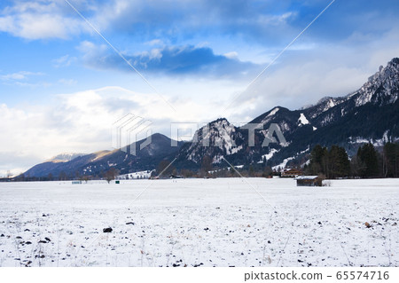 Wooden shed in snowy field against Alps in winter 65574716