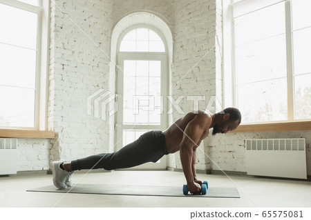 Young african-american man training at home during quarantine of coronavirus outbreak, doinc exercises of fitness, aerobic. Staying sportive suring insulation. Young african-american man training at home during quarantine of coronavirus outbreak, doinc exercises of fitness, aerobic. Staying sportive suring insulation. 65575081