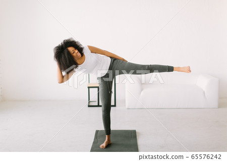 An African American young woman doing physical exercises standing in a mat An African American young woman doing physical exercises standing in a mat 65576242