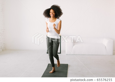 An African American young woman doing physical exercises standing in a mat An African American young woman doing physical exercises standing in a mat 65576255