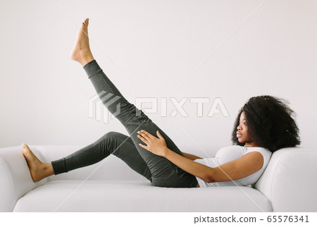 An African American young woman lying on a white bed and doing physical exercises 65576341