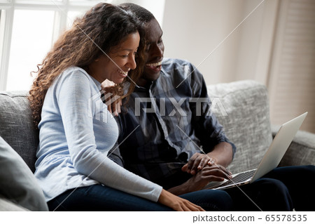 Cheerful black couple having fun in social media using laptop 65578535