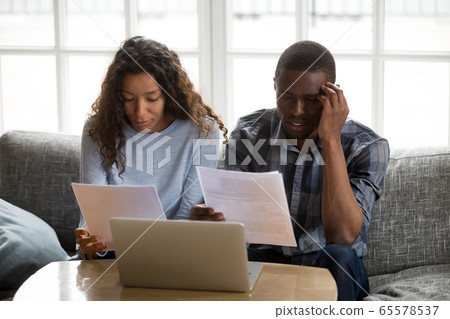 Serious concerned african american couple holding bills reading 65578537
