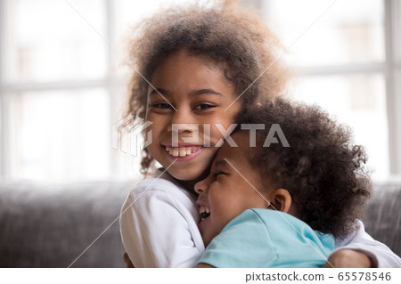 Happy african american sister embracing little brother looking a 65578546