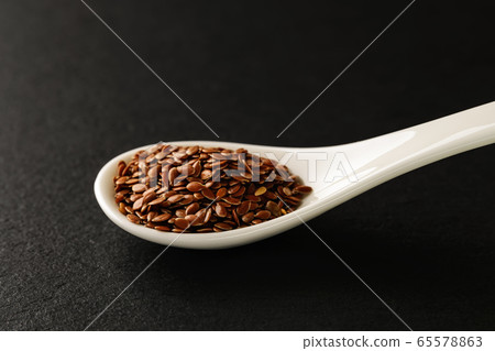 Flax seeds in a white chinese porcelain spoon on a black stone serving board. Flax seeds in a white chinese porcelain spoon on a black stone serving board. 65578863