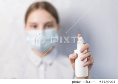 close-up focus on hand, spray antiseptic, alcohol bacteria disinfector, teenager girl in protective medical mask. Virus-safe, wash your hands, stay home. White background poster. close-up focus on hand, spray antiseptic, alcohol bacteria disinfector, teenager girl in protective medical mask. Virus-safe, wash your hands, stay home. White background poster. 65580904