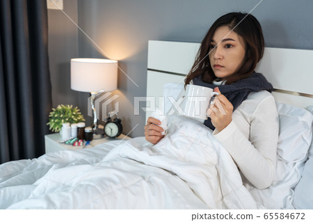 sick woman drinking a cup of hot water on bed sick woman drinking a cup of hot water on bed 65584672