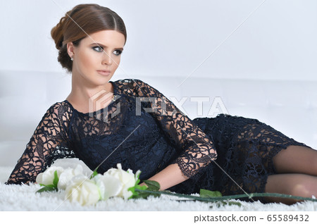 Beautiful young woman posing on bed with flowers 65589432