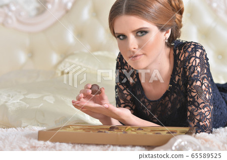 Beautiful young woman on bed with chocolates Beautiful young woman on bed with chocolates 65589525