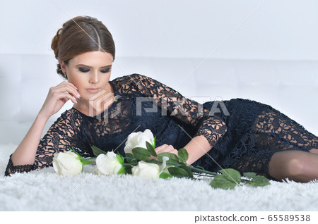 Beautiful young woman posing on bed with flowers Beautiful young woman posing on bed with flowers 65589538