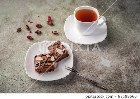 Homemade brownie with almonds on a saucer with a fork on wooden table. Next cup of tea and rose buds 65589666