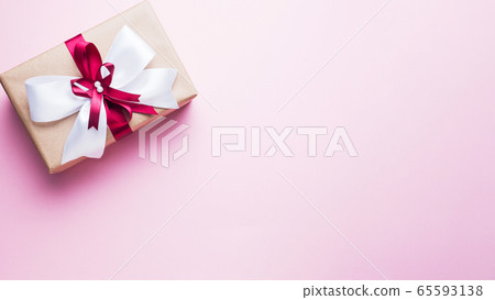 Gift or present box with a big bow on a pink table top view. Flatlay composition for Christmas birthday, mother day or wedding. 65593138