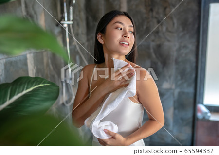 Brunette female standing in shower in night dress, wiping her shoulders with towel Brunette female standing in shower in night dress, wiping her shoulders with towel 65594332
