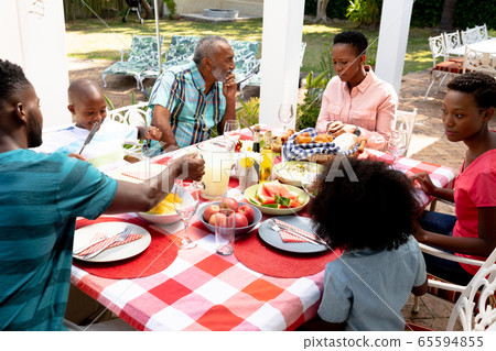 Senior African American couple and their family sitting by a table in the garden 65594855