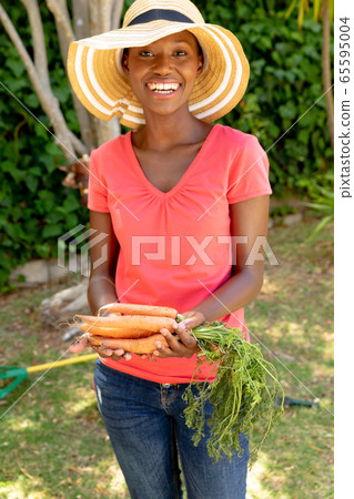 African American woman wearing gloves and presenting fresh carrots African American woman wearing gloves and presenting fresh carrots 65595004