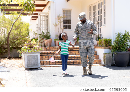 African American male soldier walking with his daughter holding a US flag 65595005