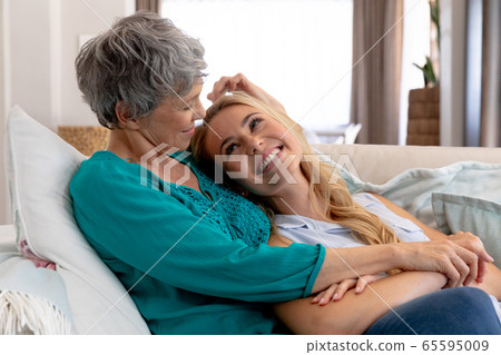 Caucasian woman and her daughter sitting on a couch and embracing at home Caucasian woman and her daughter sitting on a couch and embracing at home 65595009