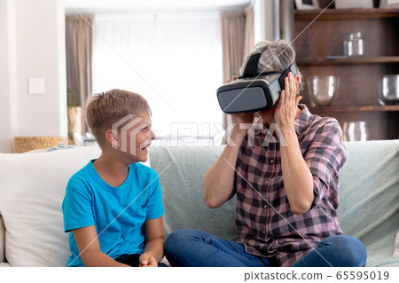 Senior Caucasian woman using a VR headset at home with his grandson Senior Caucasian woman using a VR headset at home with his grandson 65595019