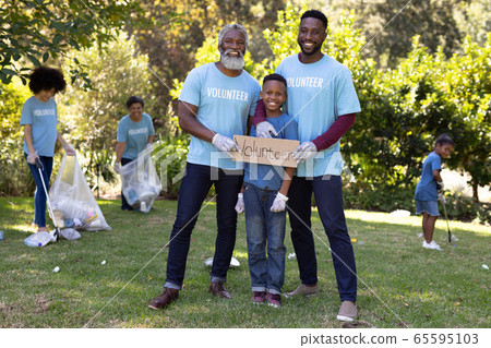 Multi-generation people collecting garbage with a boy holding a sign written Volunteer Multi-generation people collecting garbage with a boy holding a sign written Volunteer 65595103