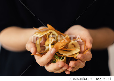 Close up hands with compost vegetable peelings on black background. Organic waste, fertilize for he 65598921
