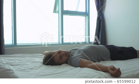 Young man lying on bed by the window in the morning at home Young man lying on bed by the window in the morning at home 65599012