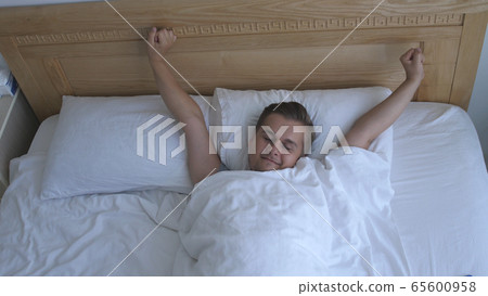 Young man stretch arm lying on bed by the window in the morning at home. Top of view Young man stretch arm lying on bed by the window in the morning at home. Top of view 65600958