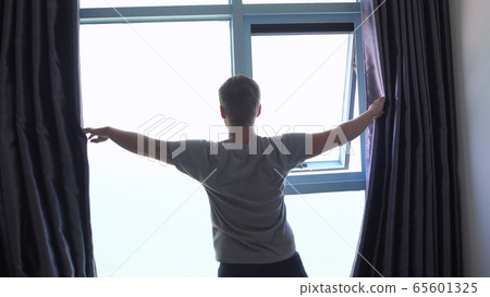 Back of view of young man unveil curtain in the morning 65601325