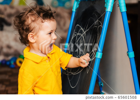 Cute baby boy learning to draw with chalk on a blackboard 65601508