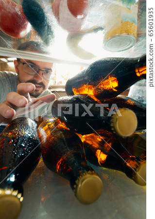 Caucasian man takes cold refreshing beer from out the fridge, inside view from fridge of hand holding the bottle Caucasian man takes cold refreshing beer from out the fridge, inside view from fridge of hand holding the bottle 65601935