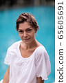 Pretty woman with sort haircut sitting near pool 65605691