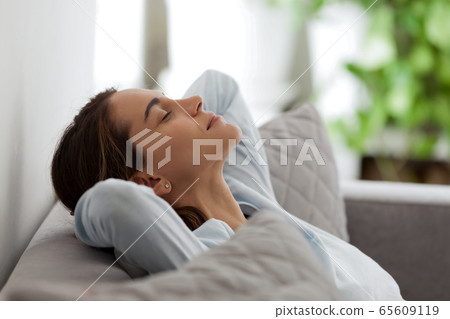 Happy satisfied mixed race female freelancer relaxing on comfortable sofa. 65609119