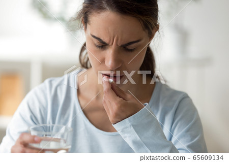 Unhappy lady feeling unwell, getting aspirin or painkiller. Unhappy lady feeling unwell, getting aspirin or painkiller. 65609134