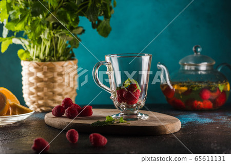 glass cup with raspberry tea mint leaves and lemon on blue 65611131