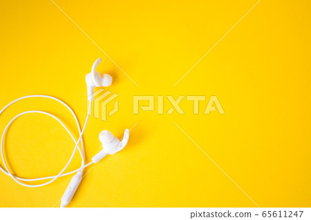 White headphones with a wire on a yellow background. Concept of gadgets. White headphones with a wire on a yellow background. Concept of gadgets. 65611247