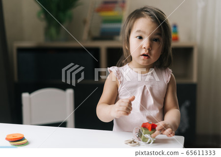 Pretty beautiful little two-year-old girl is playing with educational toy standing at the table Pretty beautiful little two-year-old girl is playing with educational toy standing at the table 65611333