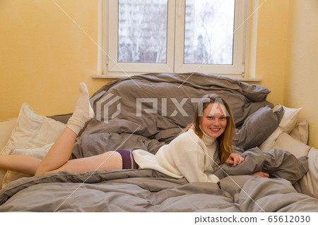 Girl in warm sweater and panties lies across bed Girl in warm sweater and panties lies across bed 65612030