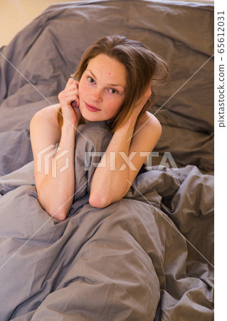 Young girl sitting in bed alone, hiding in blanket Young girl sitting in bed alone, hiding in blanket 65612031