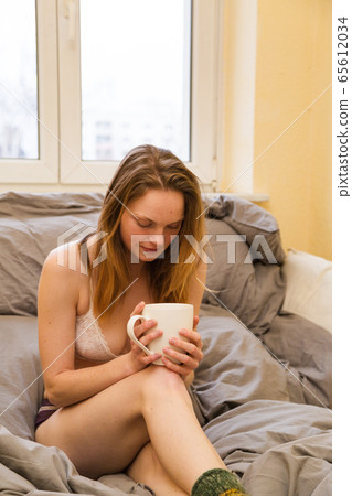 Woman in underwear drink beverage sitting on bed Woman in underwear drink beverage sitting on bed 65612034