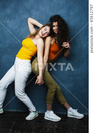young pretty teenage girls friends with blond and brunette curly hair posing cheerful on blue background, lifestyle people concept 65612797